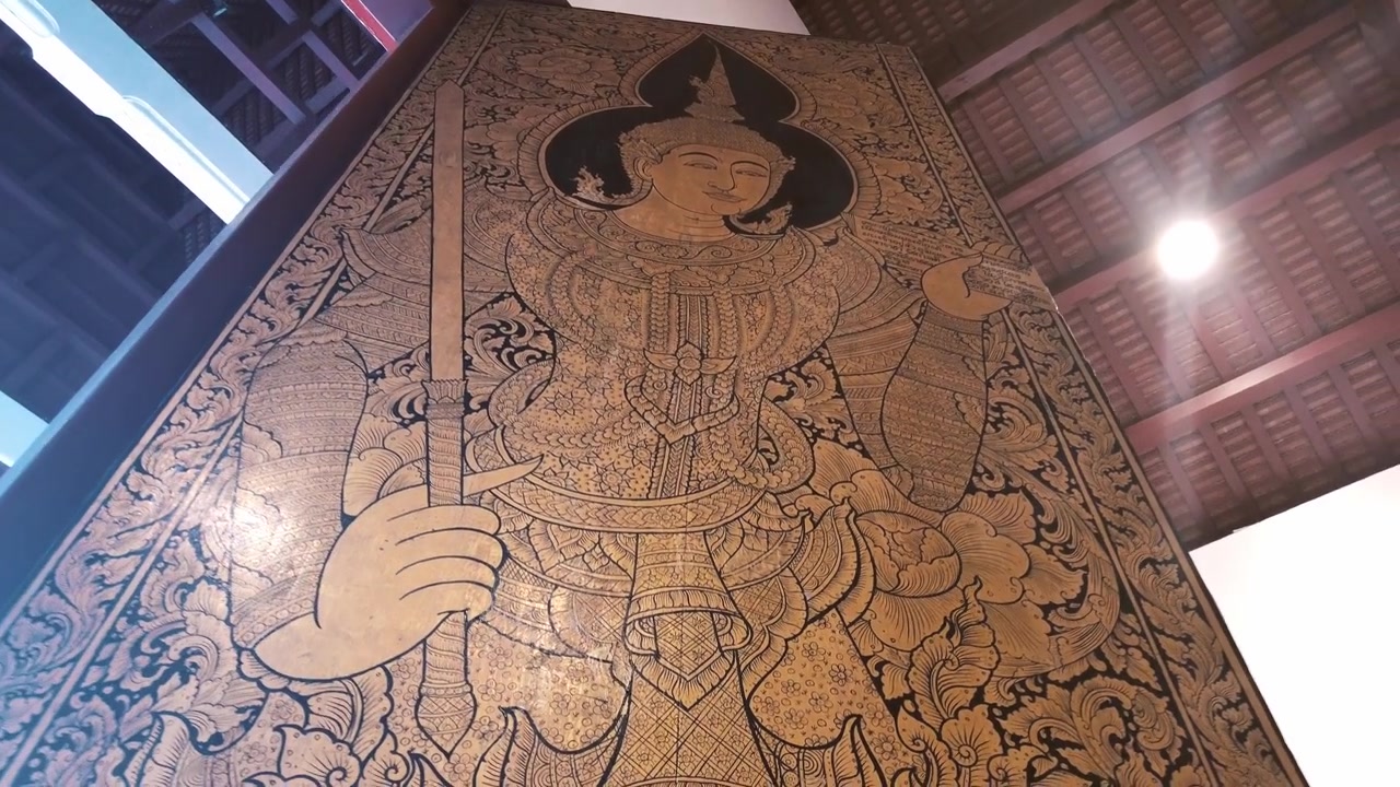 Enorme porta di tempio con intaglio tradizionale thailandese in legno dipinto, raffigurante un angelo o una divinità celeste (devata) che impugna una spada