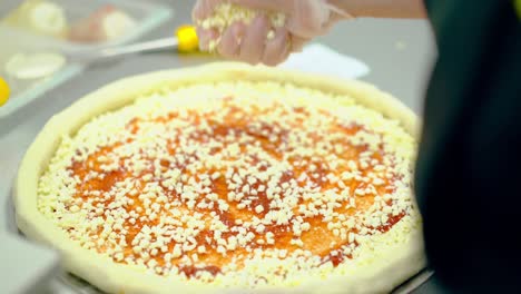 cu cook prepares pizza sprinkles it with cheese