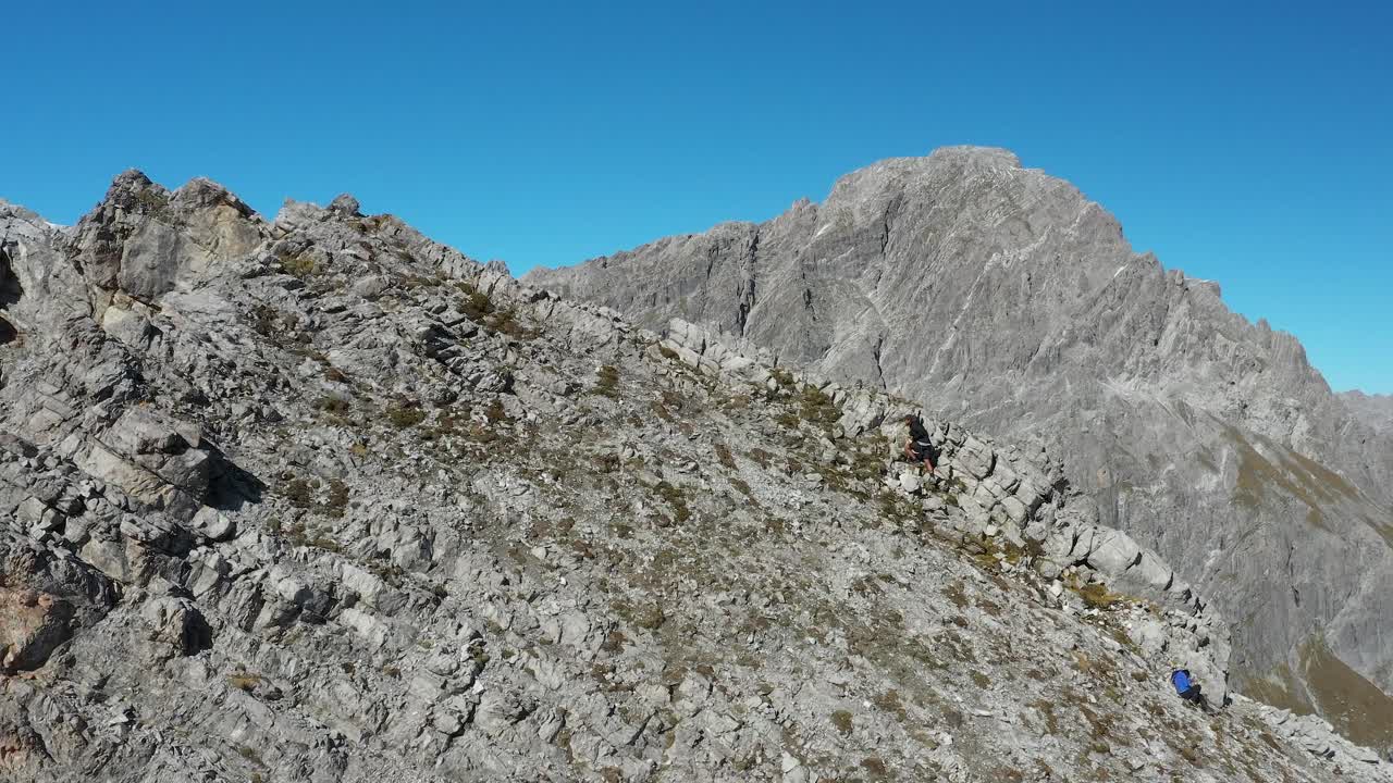 un hombre está subiendo por la ladera de un pico de montaña con un amigo sentado debajo