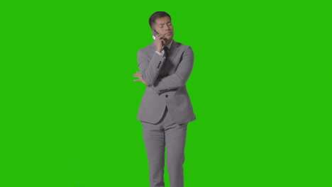 three quarter length studio shot of businessman in suit taking mobile phone call against green screen