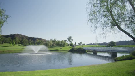 Pan-A-La-Izquierda-Amplia-Vista-De-Un-Campo-De-Golf-Con-Una-Fuente,-Lago-Y-Puente