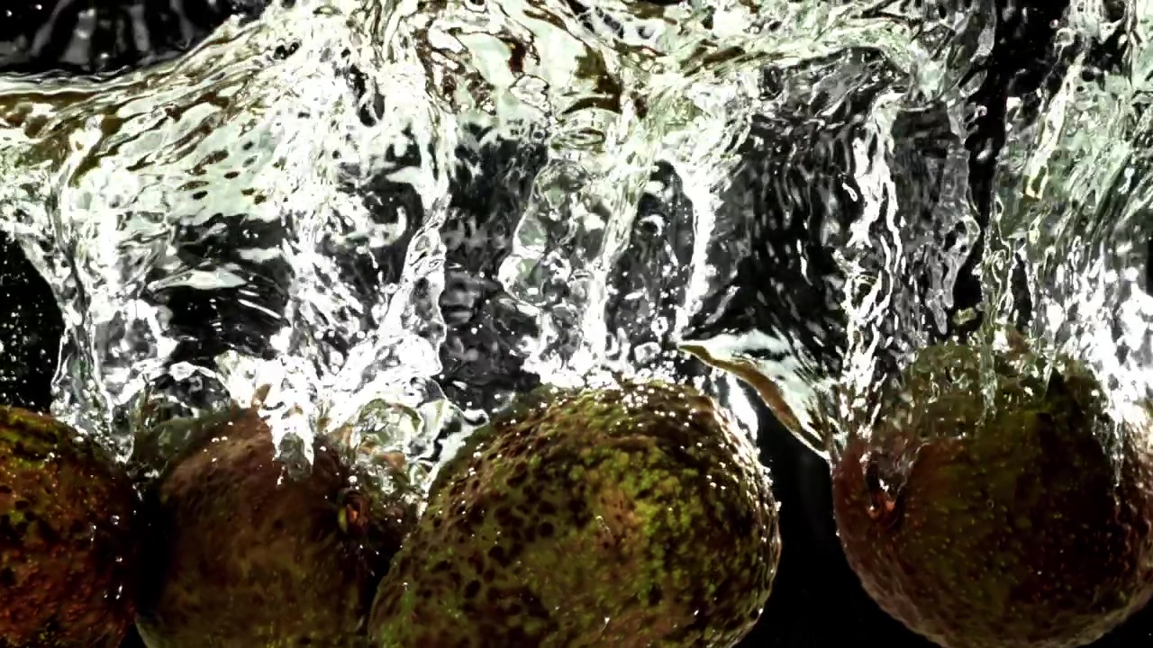 Friske avocadoer plasker ned i klart vand på sort baggrund