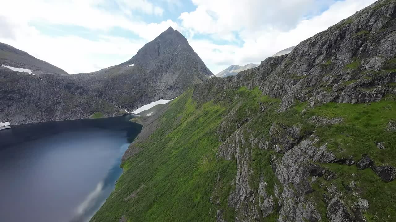 FPV drone glides over a tranquil mountain lake, leading to a majestic peak, capturing the serene beauty of nature's grandeur in motion