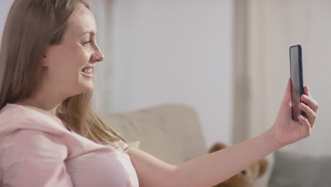 Mujer-Embarazada-Sentada-En-El-Sofá-En-Una-Videollamada-Usando-Un-Teléfono-Inteligente