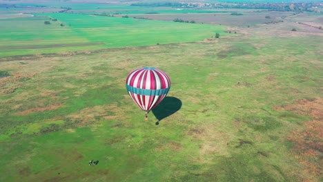 flying around colorful air balloon which is about to take off from a green field