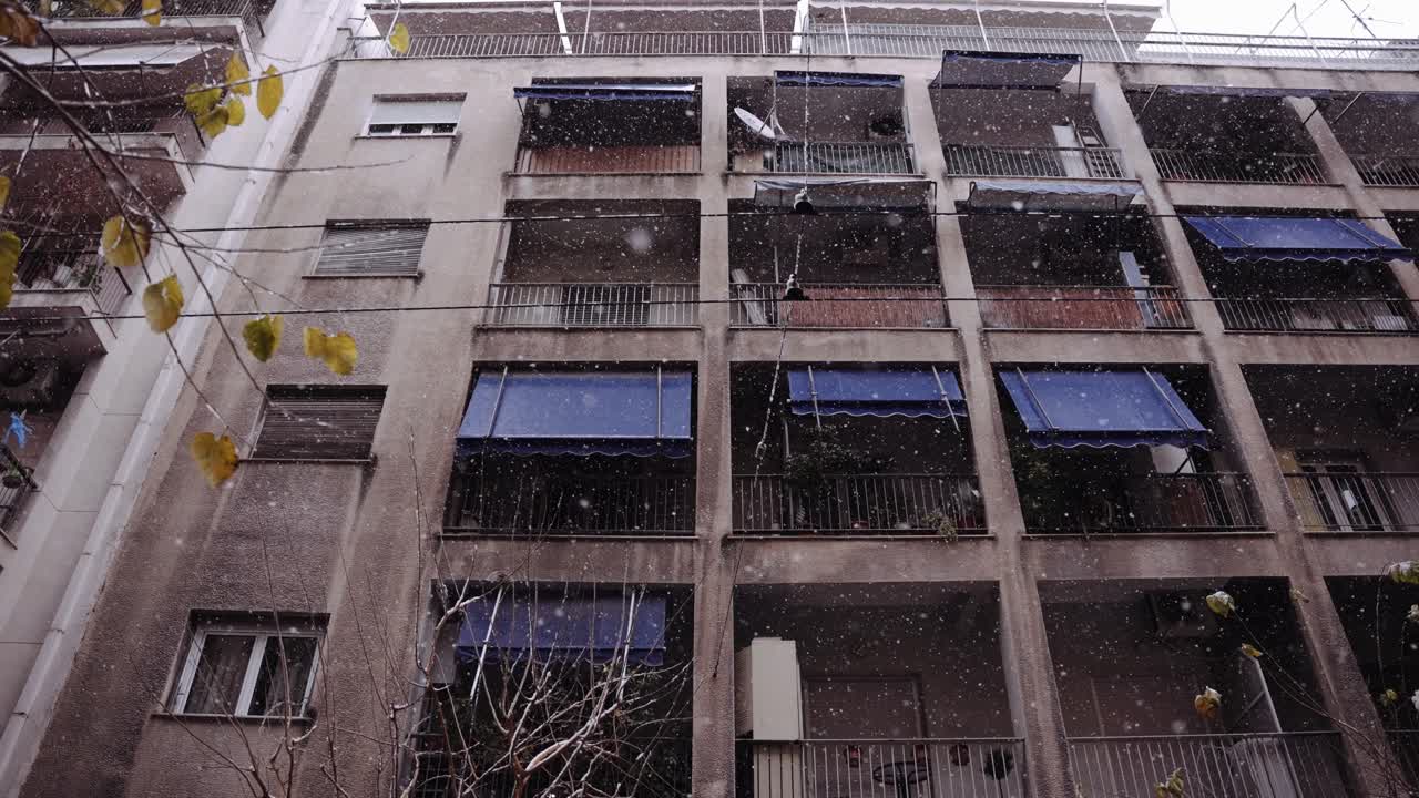 copos de nieve en cámara lenta cayendo con un gran edificio de apartamentos en el fondo, ciudad de atenas