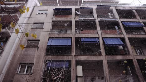 Schneeflocken-In-Zeitlupe-Fallen-Mit-Einem-Großen-Wohnhaus-Im-Hintergrund,-Athener-Stadt