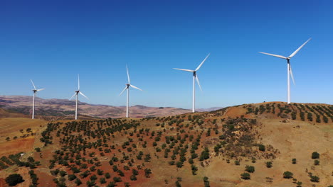 4k aerial view of 5 wind turbines making alternative energy, renewable energy source, blue sky farm lands