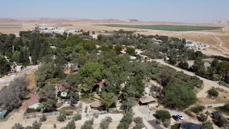 aerial backwards panoramic drone shot of kibbutz sde-boker, filled with trees, bushes, fields, trails, buildings and houses