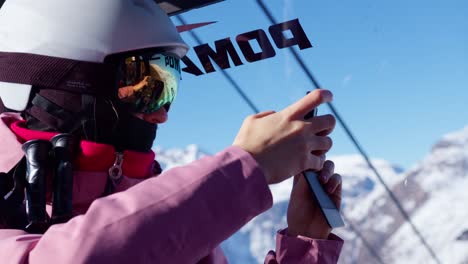 skier woman taking cell phone photos of snowy mountain scenery from inside the cableway