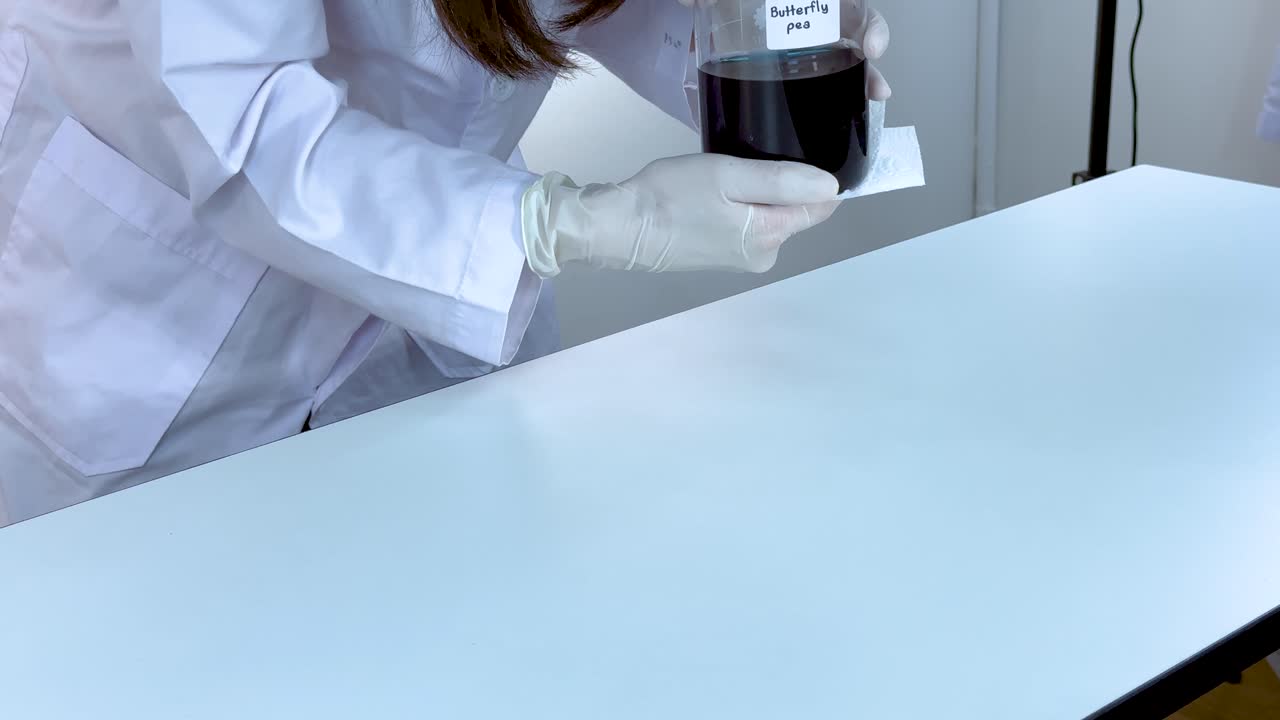 실험실 기술자 는 밝은 조명 아래 어두운 액체 를 담은 컵 으로 과학 실험 을 준비 하면서 테이블 을 고 있다