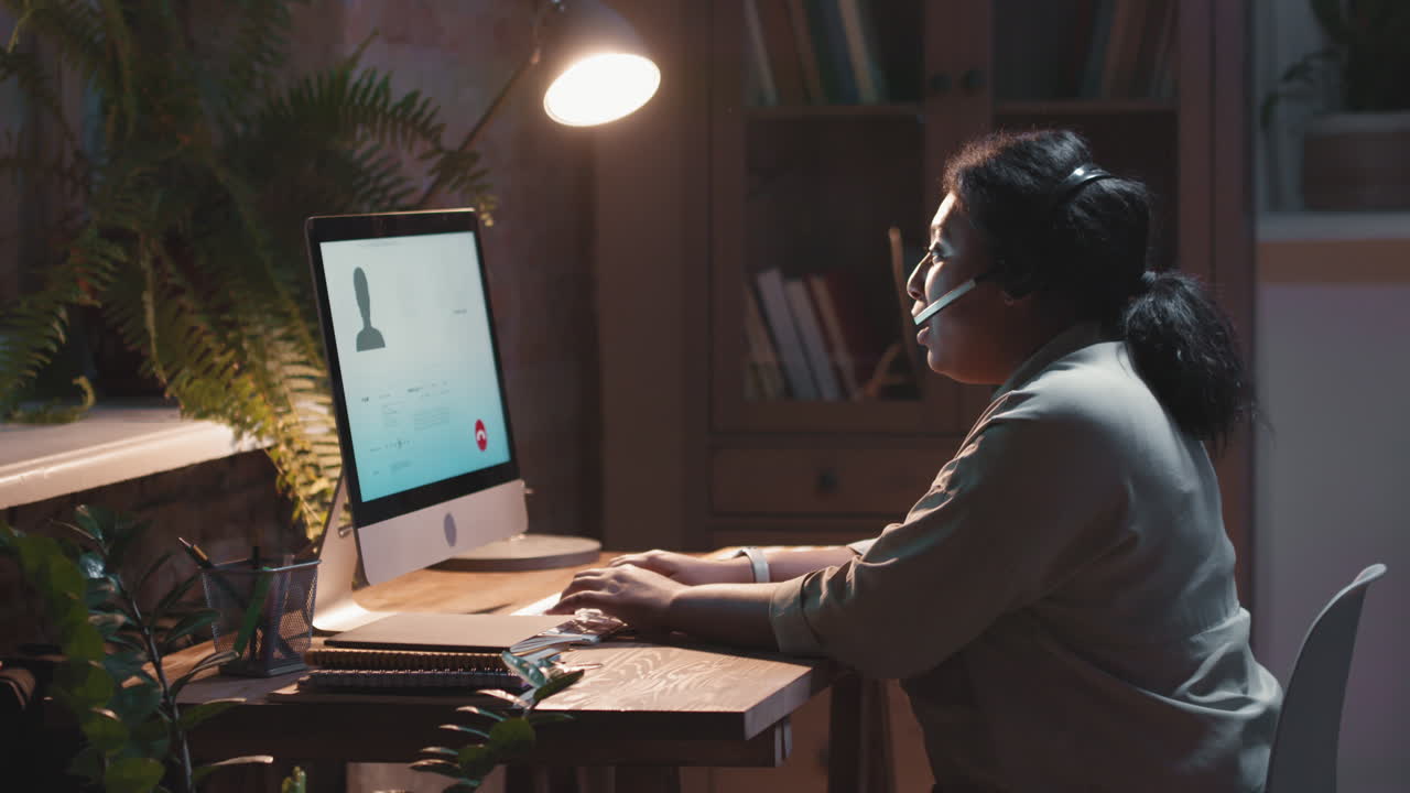 Kvinde på videomøde arbejder hjemmefra med headset og computer i et dæmpet rum