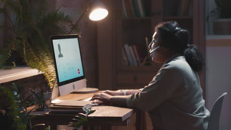 woman on a video call working remotely with a headset and computer in a dim room