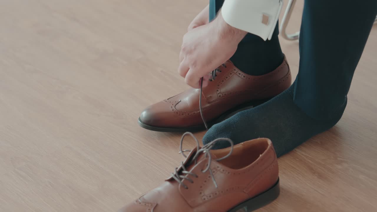 Nærbillede af hænder, der snører brune sko på trægulv