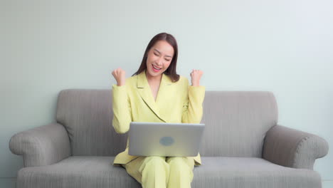 while working on her laptop, a young, pretty businesswoman in a yellow suit, reacts non verbally to her success