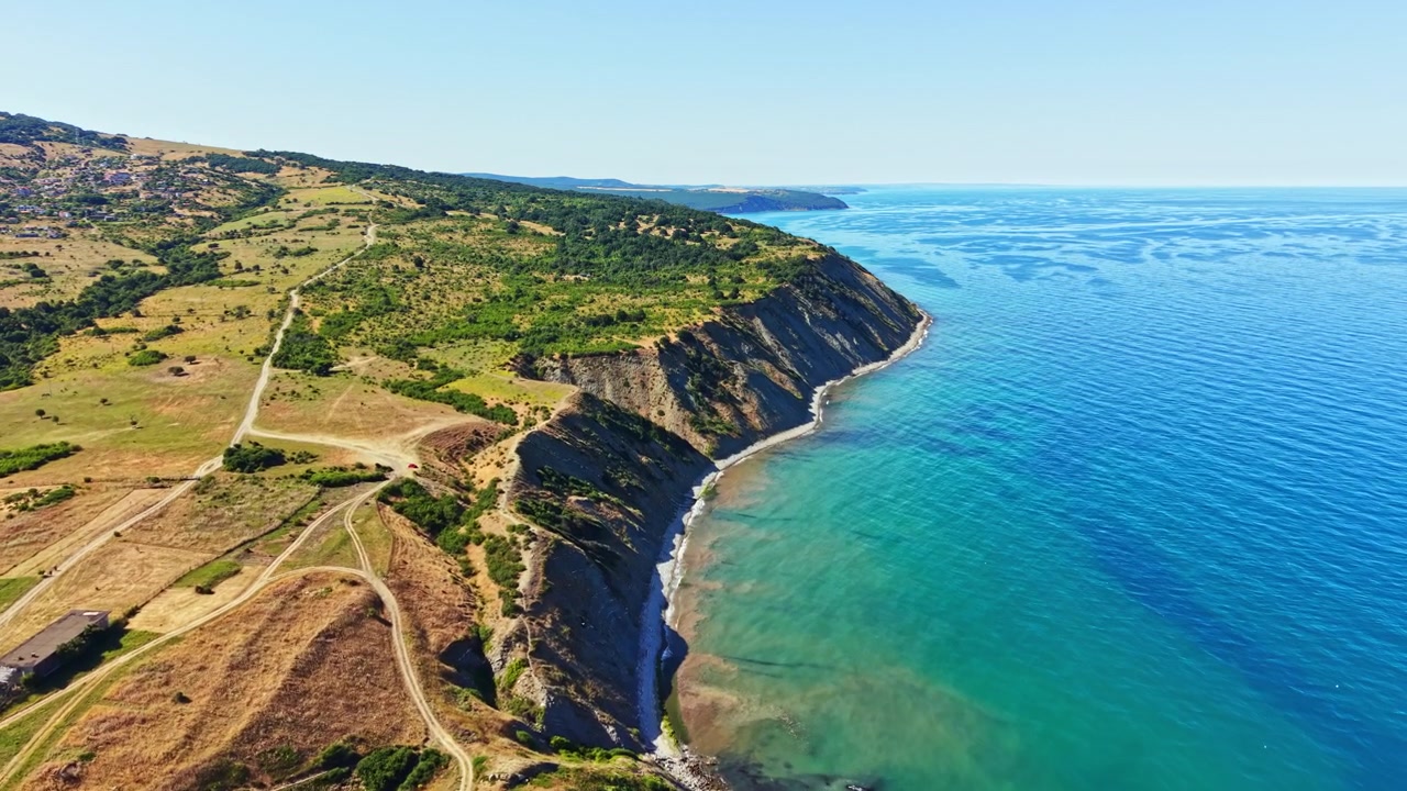 Uzak bir konumda, gündüz saatlerinde, berrak gökyüzü altında falezler ve deniz ile kıyı şeridi manzarası