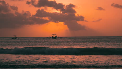 indonesian outrigger boats in silhouette floating in sea against golden sunset in jimbaran beach, bali indonesia