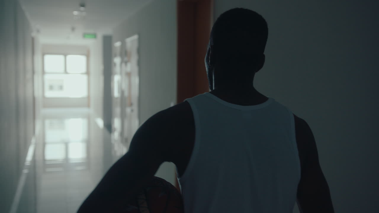 Giocatore di basket nero che cammina con un pallone lungo un corridoio