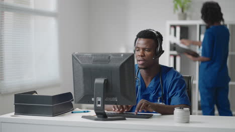 médico o enfermera afroamericano con auriculares y computadora trabajando en el hospital .joven médico terapeuta profesional consultando al cliente usando comunicación remota hablando por cámara web