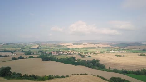 Drone-Acercándose-A-Un-Pequeño-Pueblo-En-La-Cima-De-Una-Colina-De-Toscana,-Paisaje-Tradicional-Italiano-Con-Carreteras-Y-Cipreses-De-Tierras-De-Cultivo-En-Colinas