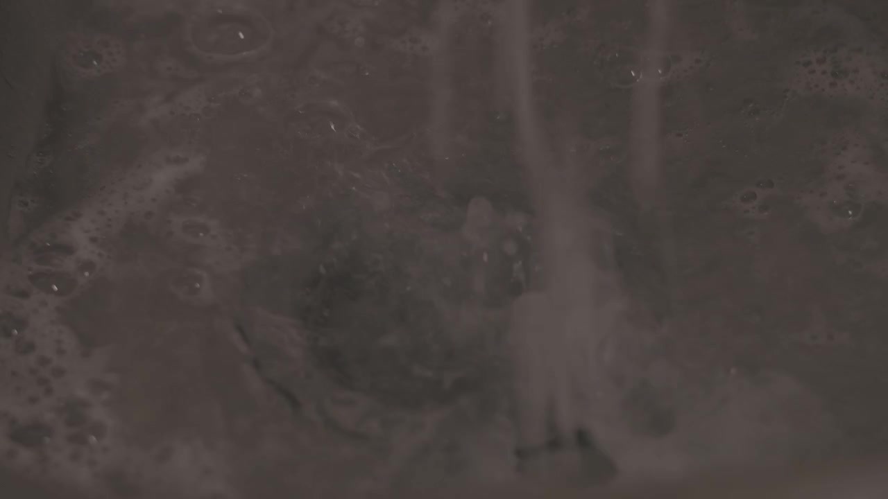 Close-up shot of soapy water flowing down a kitchen sink as hands wash dishes