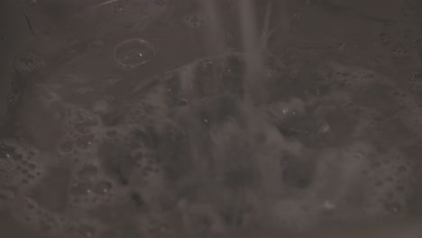 Close-up shot of soapy water flowing down a kitchen sink as hands wash dishes