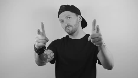 slow motion footage of a man with tattoos and a cap on his head lifts up his arms and points at the camera with confidence and approval while on a white background with shadows