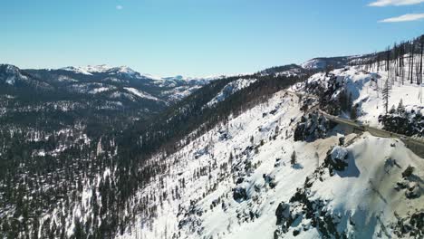 Aerial-drone-view-of-high-altitude-mountain-highway-and-valley-below-in-winter