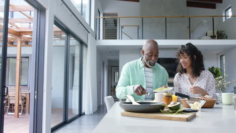 Happy-biracial-couple-having-scrambled-eggs-for-breakfast-in-kitchen,-slow-motion