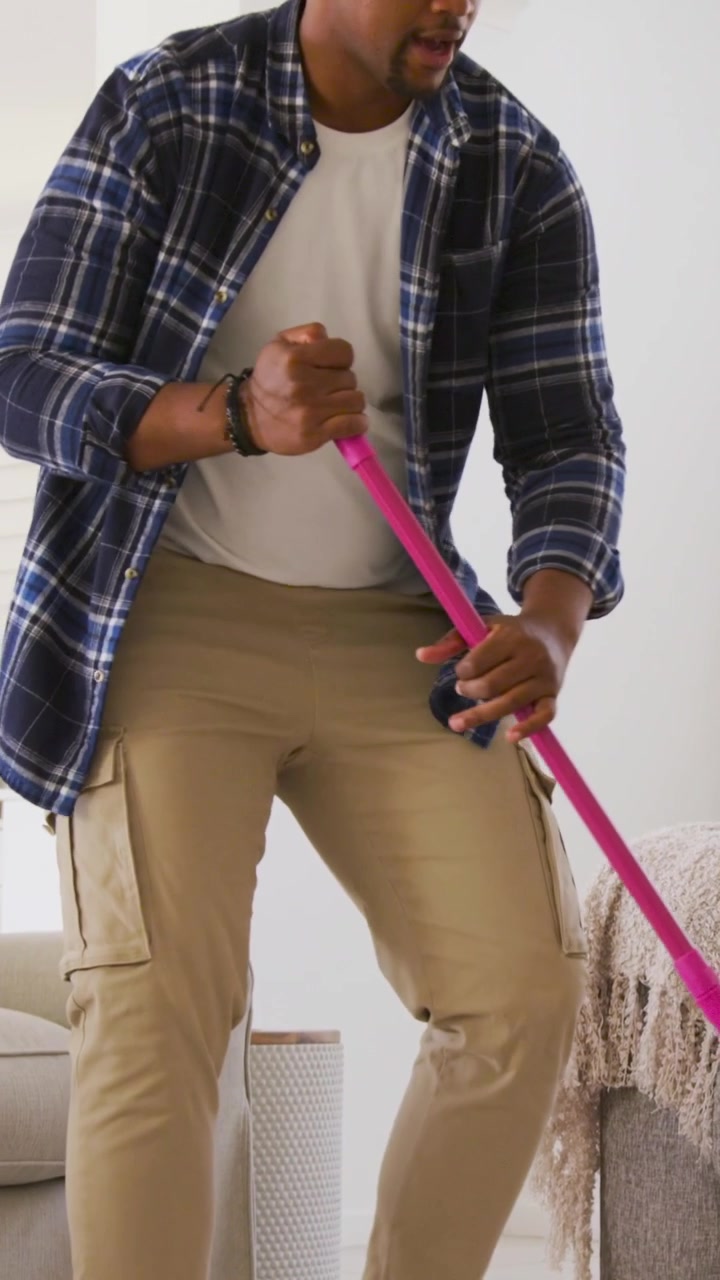 Video verticale: Uomo in camicia a quadri che spruzza una bottiglia blu e poi lava il pavimento con un mop in soggiorno.