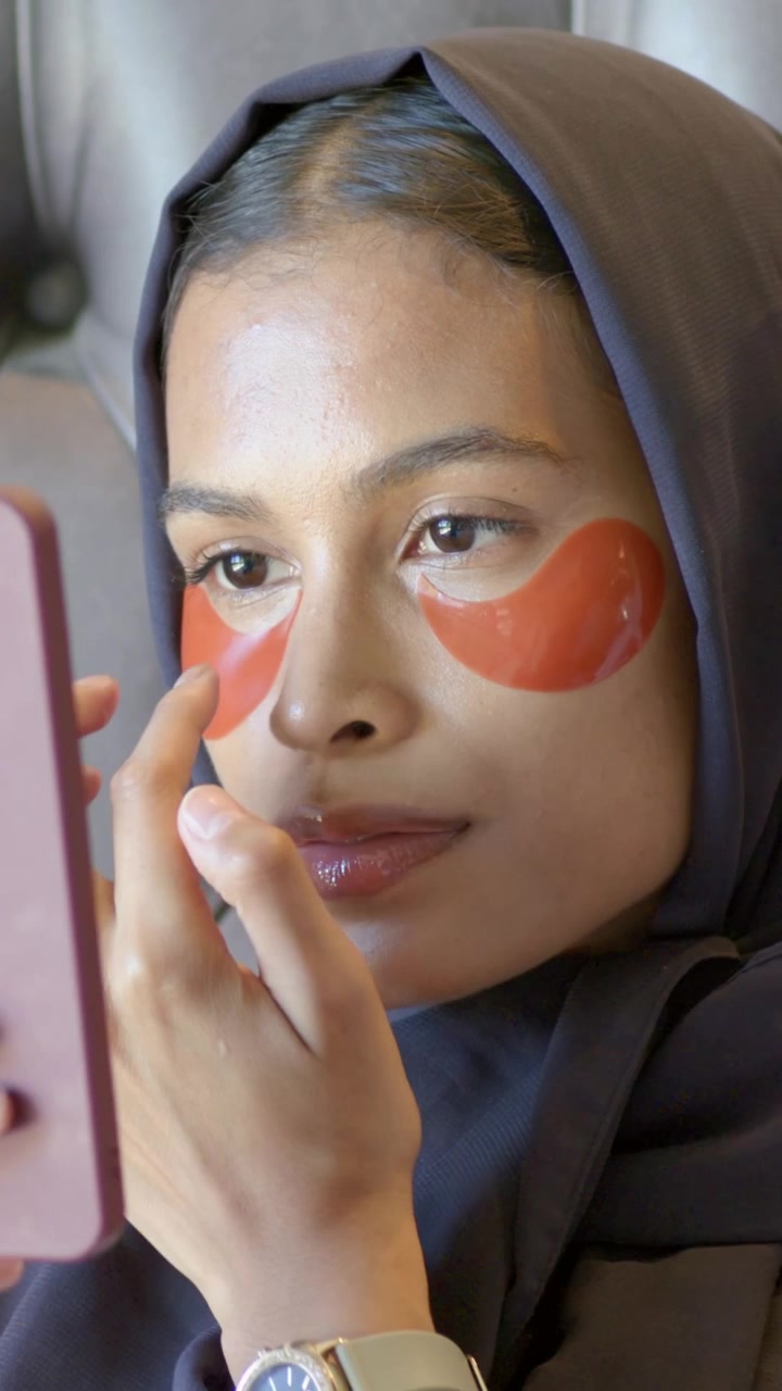 Vertical video: Bringing device, woman in hijab in bed checking and tapping eye pads, copy space