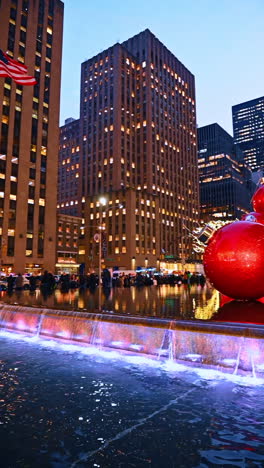 New York, USA, 20 December 2025: NY plaza bustling at night. Crowds gather around a sparkling fountain in New York as evening lights illuminate the surrounding buildings