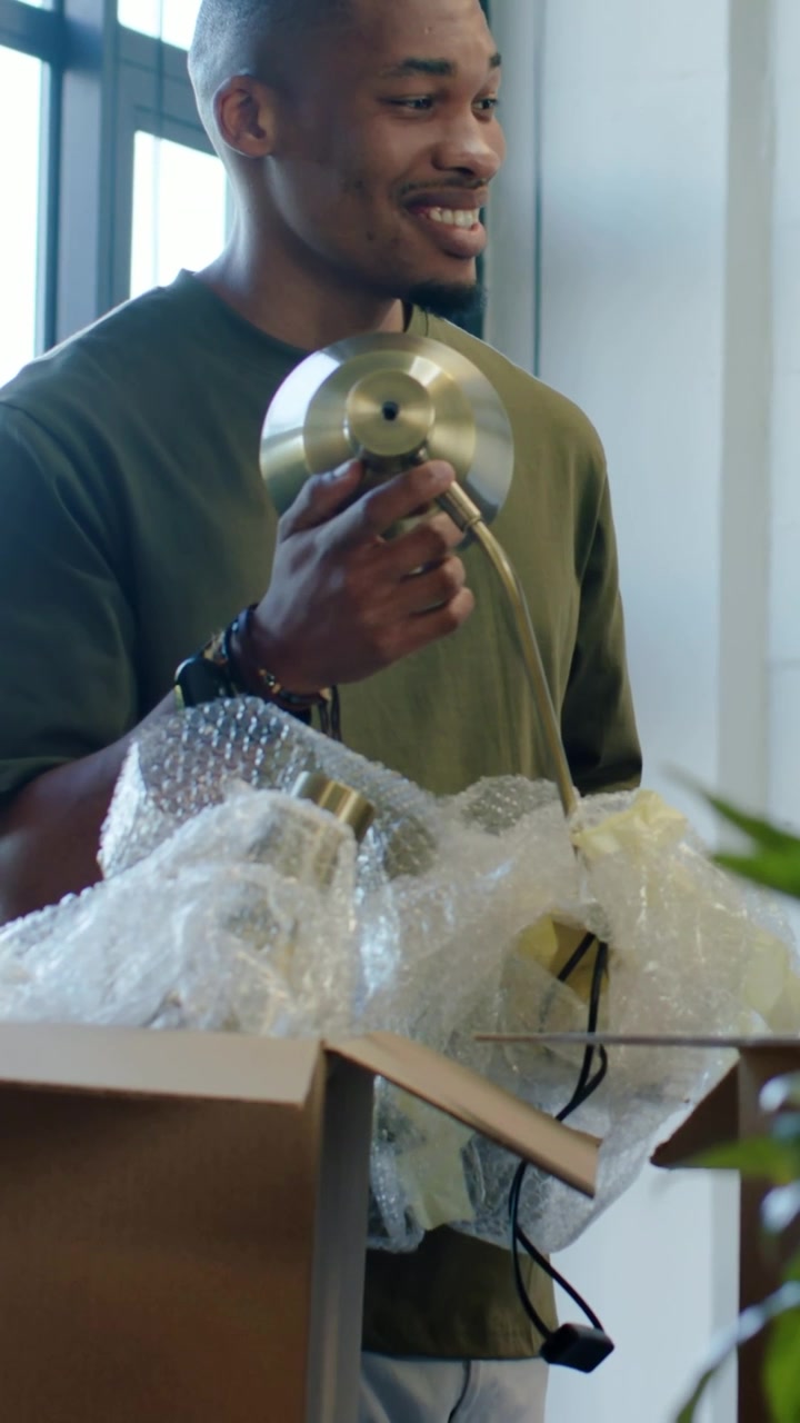 Vertical video: Unpacking man in olive shirt lifting brass fixture at home, preparing to assemble