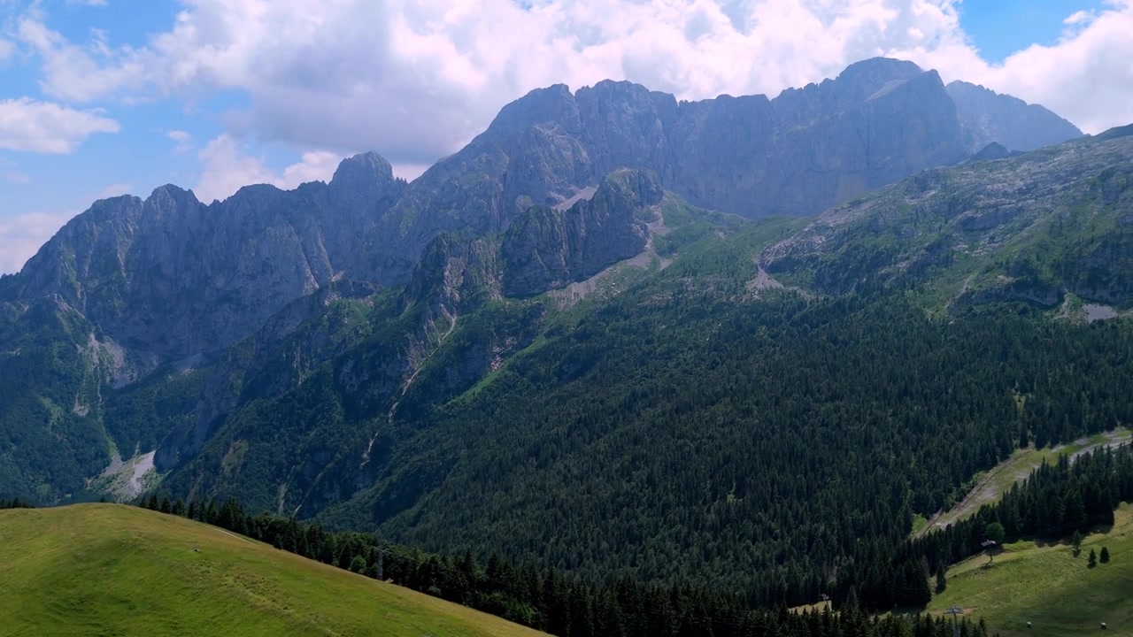 Aerial drone perspective overlooking the majestic Mount Presolana and lush green alpine slopes in Val di Scalve, Italian Alps, Italy, capturing the rugged mountain terrain.
