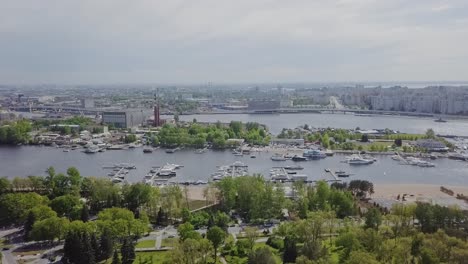 Parte-Portuaria-De-La-Ciudad-Con-Muchos-Barcos,-Yates,-Fábrica-En-El-Fondo,-Panorama-De-La-Ciudad,-Parque-Industrial-Verde-Y-árboles