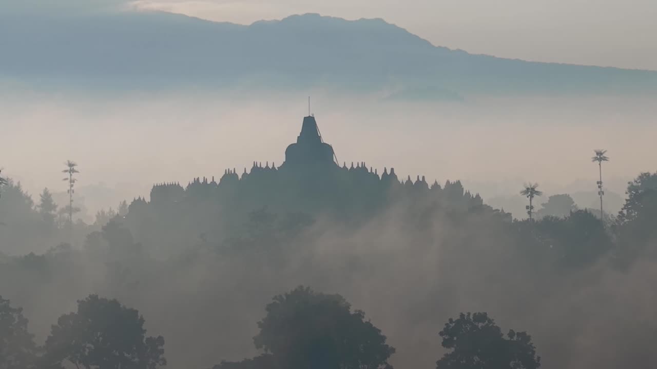 Splendida alba nebbiosa al Tempio di Borobudur con nebbia leggera e foresta lussureggiante, creando un paesaggio indonesiano pacifico e suggestivo.