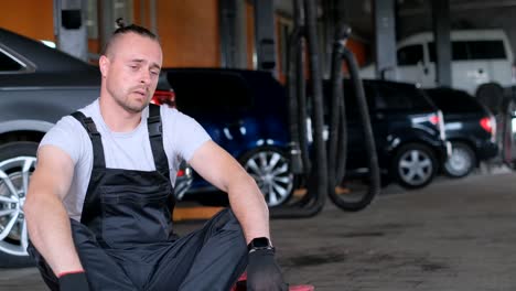 tired mechanic sitting on the floor in a car repair shop