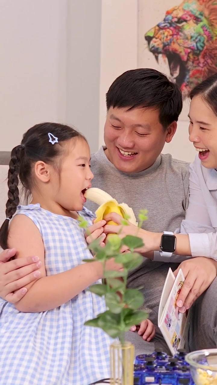 Cha mẹ mỉm cười và con gái nhỏ của họ chia sẻ khoảnh khắc vui đùa ăn trái cây tại nhà.