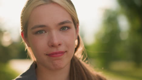 close-up of lady looking directly at camera with subtle smile, warm sunlight glowing softly from behind, her face is illuminated in natural light, with greenery and a blurred background