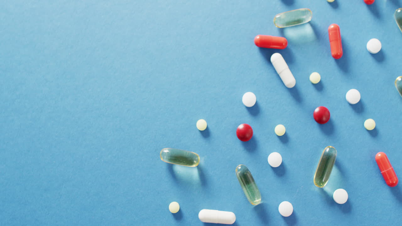 Video of a variety of pills and capsules on blue background with copy space