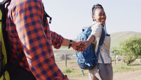 happy african american couple with backpacks, hiking together on sunny day, slow motion