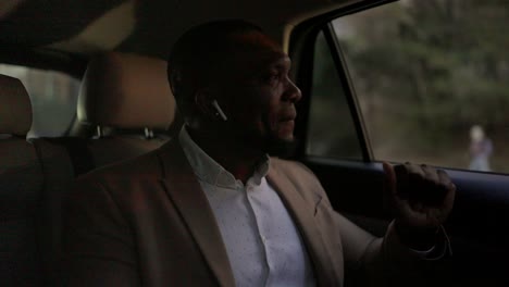 a cheerful and happy man with black skin and a beard in wireless headphones listens to music and dances while driving in the passenger seat in the modern interior of a modern car