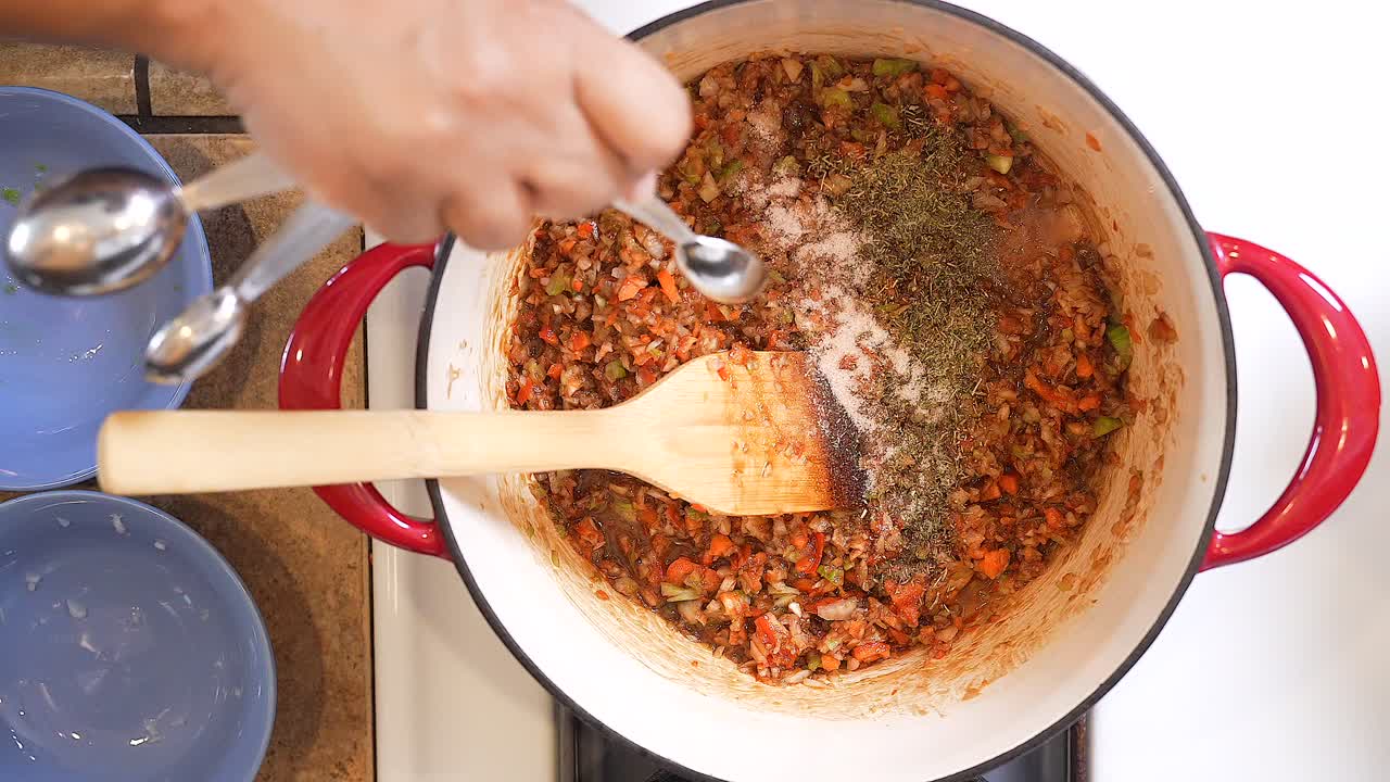 agregando sal al roux mientras hierve a fuego lento para preparar la salsa para un gumbo de salchicha andouille y mariscos - serie gumbo de vista superior