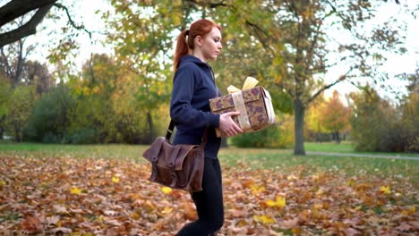 a young woman dressed in casual attire strolls through a park filled with fallen leaves, holding a beautifully wrapped gift. the vibrant autumn colors create a serene atmosphere as she walks.