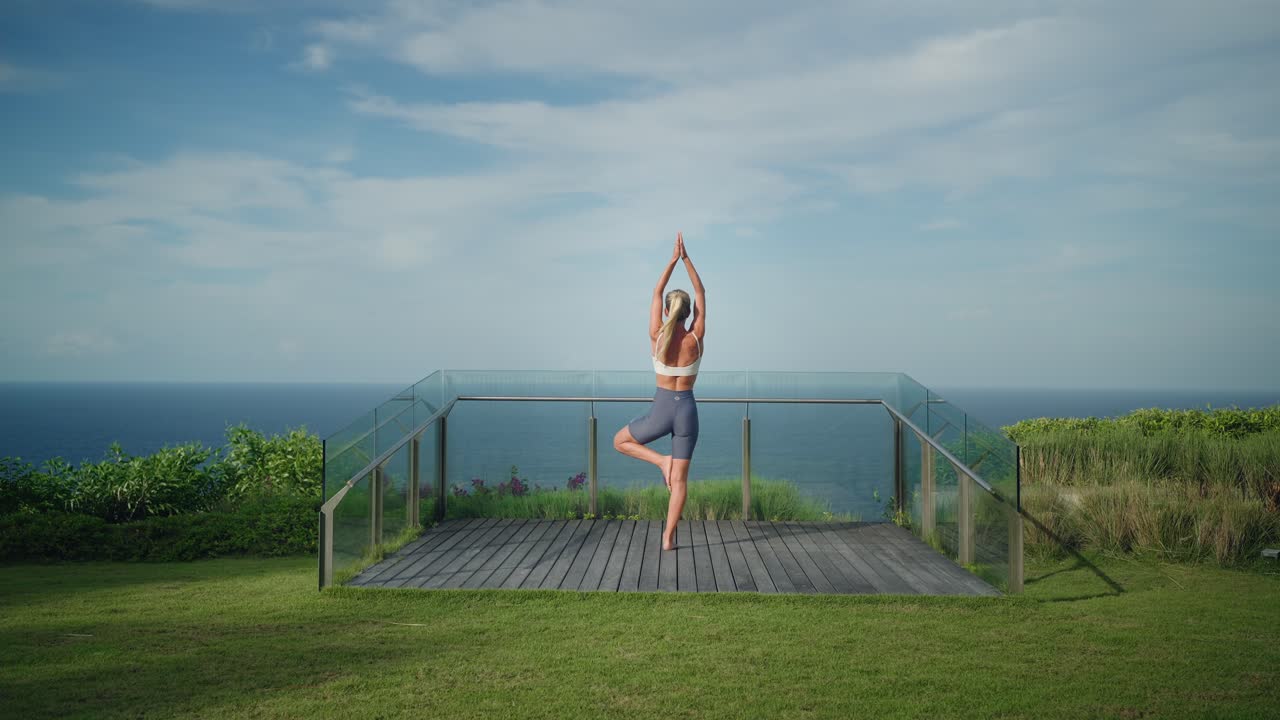 colocar joven mujer rubia haciendo pose de árbol en la plataforma de observación del acantilado, bali