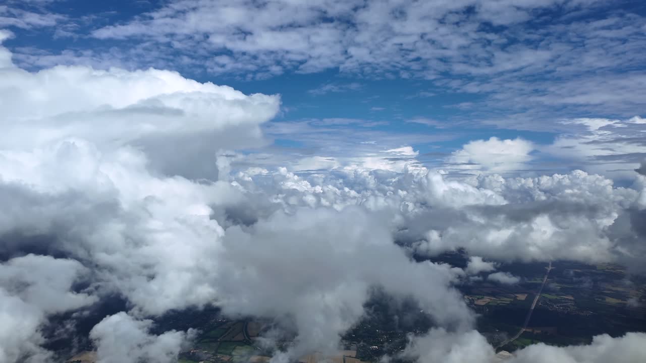 An aerial view through the pilot’s eyes taken from a jet cockpit while flying among towering storm clouds over the ground, under a blue sky. ultra-realistic 4K shot