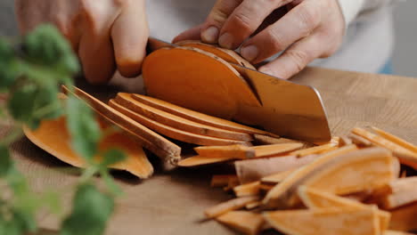chef masculino cortando camote en rodajas finas en la cocina en una tabla de cortar de madera en la cocina