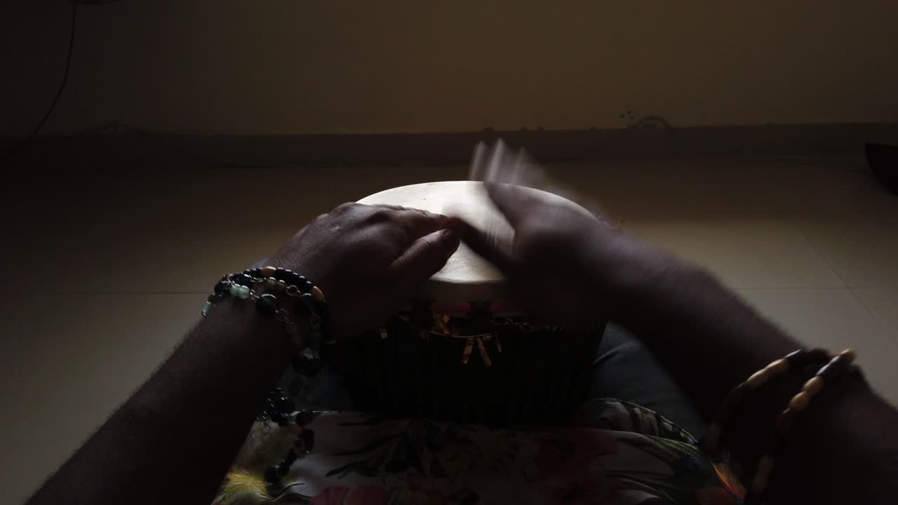 средний широкоугольный снимок мужчины, играющего на барабане джембе в одиночестве в темной комнате