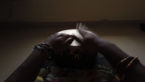 Medium-wide-looking-down-isolated-shot-of-a-man-playing-djembe-drum-alone-in-a-dark-room