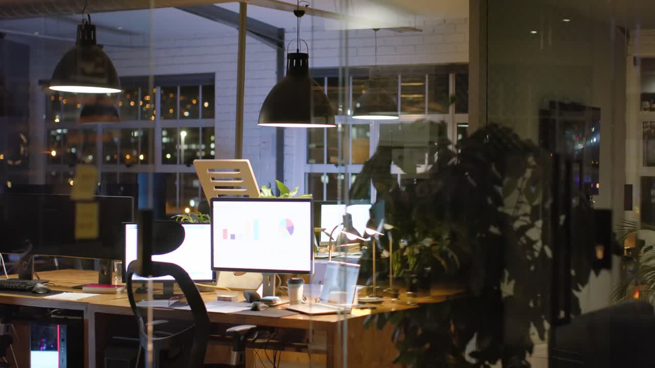 Interni dell'ufficio con le luci accese di notte, con piante, scrivanie e computer, al rallentatore.